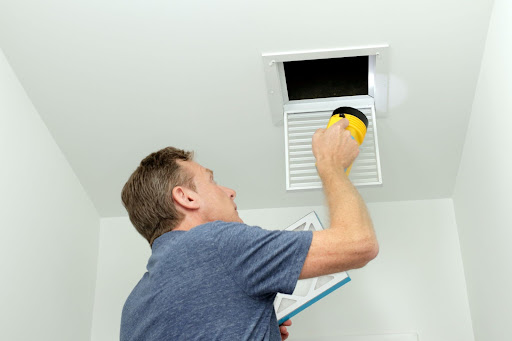 A HVAC professional inspecting an air duct for an air duct replacement.